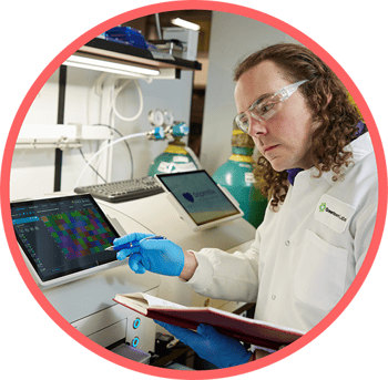 Man with labcoat and blue gloves looking at screen holding a book